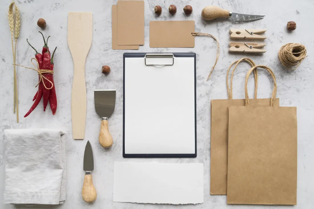 Materiales de un negocio pequeño ordenados sobre una mesa clara: tarjetas, delantal, taza y teléfono