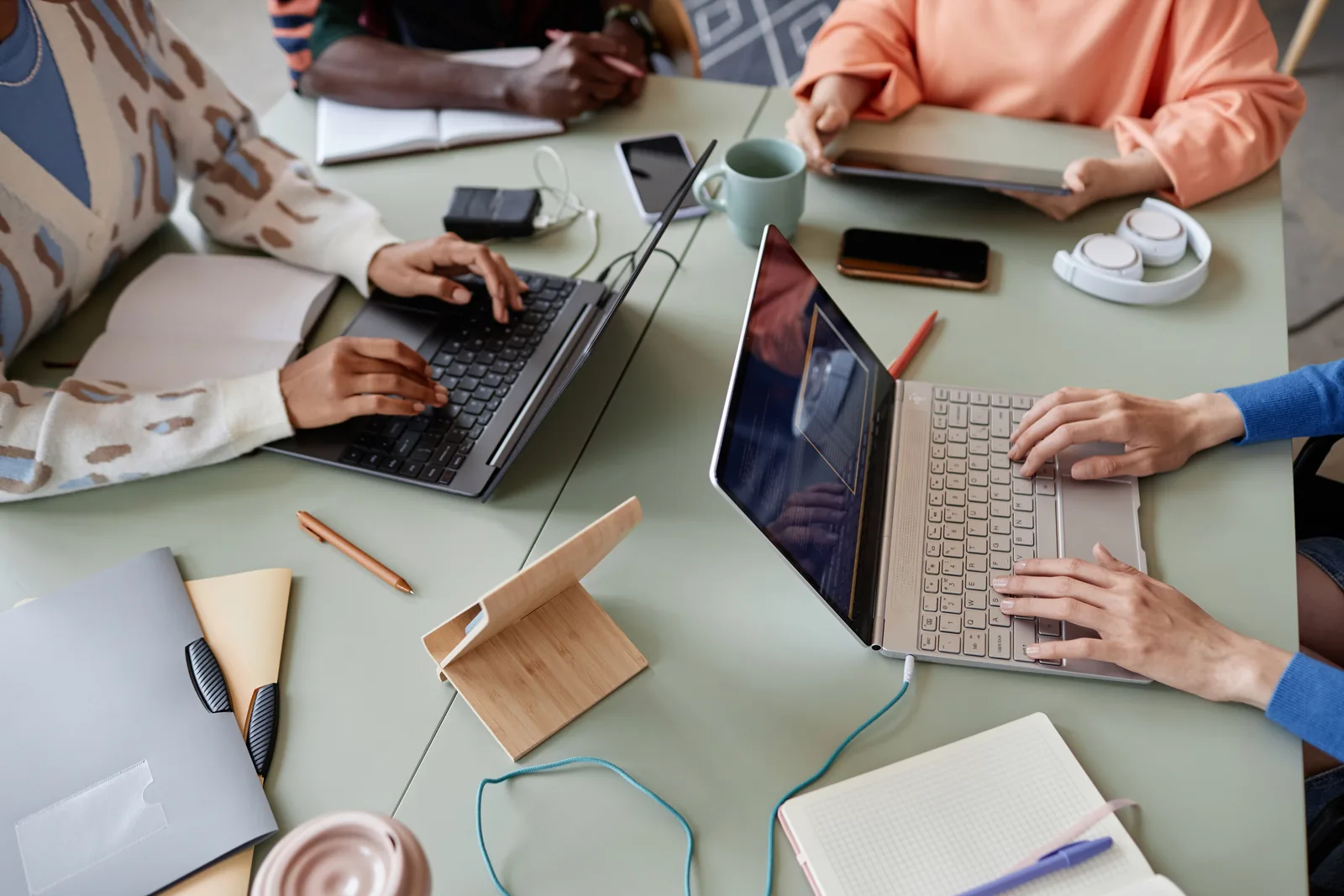 Varias personas trabajan con sus portátiles alrededor de una mesa, vistas desde arriba